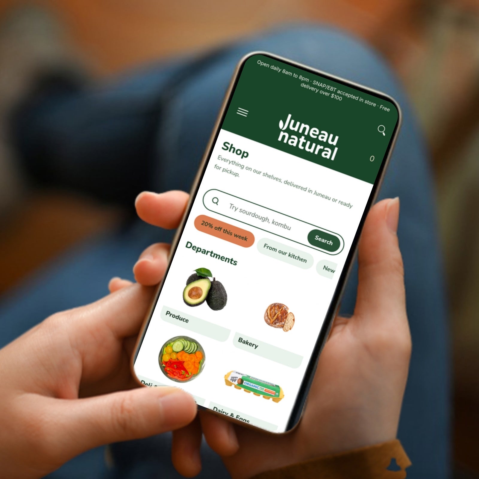 A hand holding a phone showing the Juneau Natural Shop page